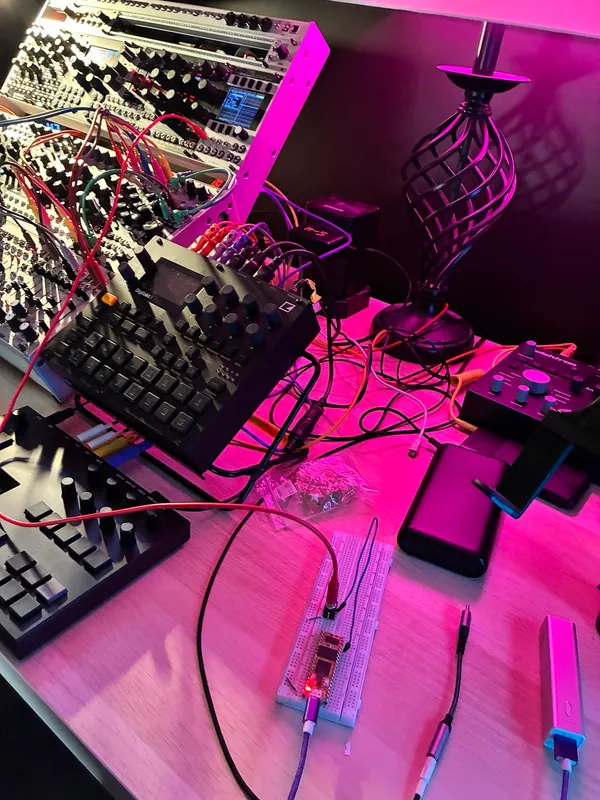 Breadboard prototype on the studio desk in front of a Eurorack case and a Digitakt, under pink light